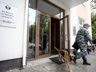 Сотрудник полиции со служебной собакой покидают офис РАО. Москва, 27 июня 2016 года