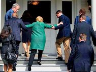 Охрана Хиллари Клинтон помогает ей пройти по ступенькам.