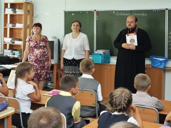Представитель РПЦ передает светской школе учебники по основам православной культуры.